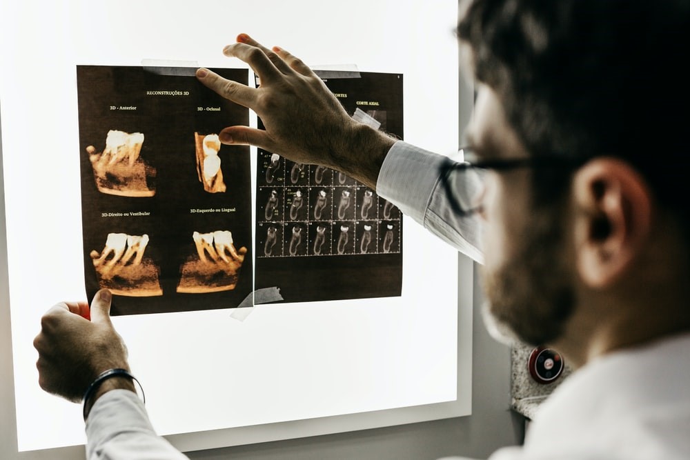 A male dentist holding up teeth scans against a tablet computer