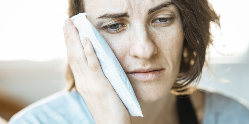 A woman holding an ice pack against her cheek.
