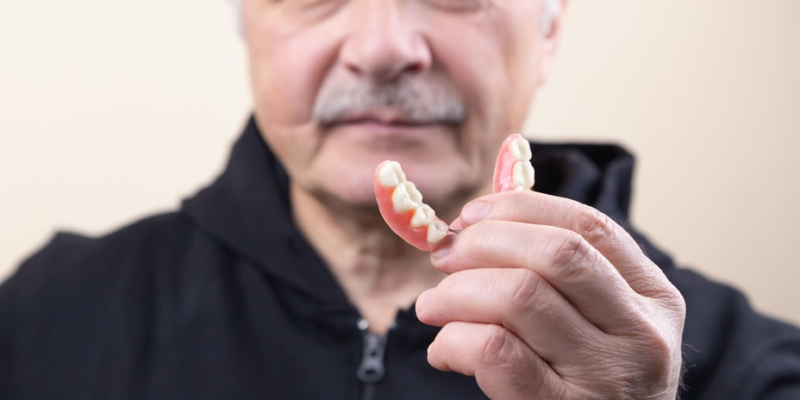 An old man showing a partial denture in his hand.